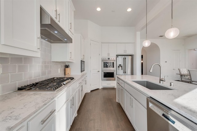 kitchen featuring arched walkways, light stone countertops, stainless steel appliances, under cabinet range hood, and a sink