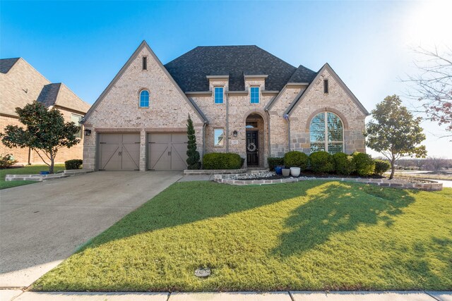 french provincial home featuring a yard, roof with shingles, concrete driveway, and brick siding