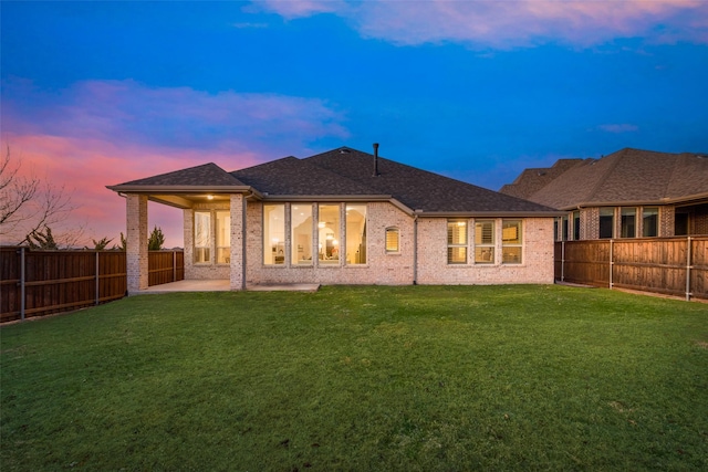 rear view of property with brick siding, a fenced backyard, a lawn, and a patio