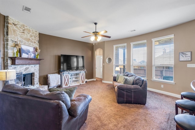 living room featuring arched walkways, a stone fireplace, carpet flooring, visible vents, and baseboards