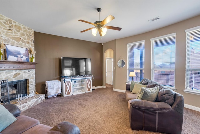 carpeted living area featuring arched walkways, a fireplace, visible vents, a ceiling fan, and baseboards