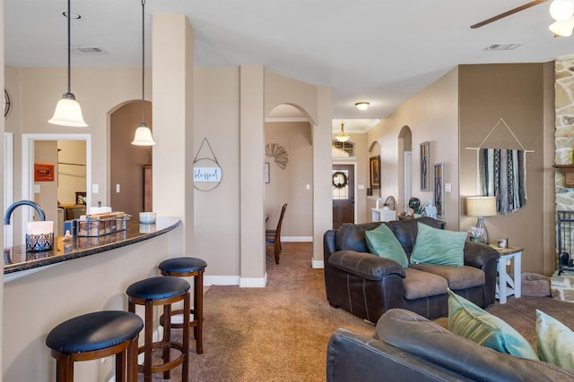 living room with arched walkways, visible vents, a ceiling fan, carpet flooring, and baseboards