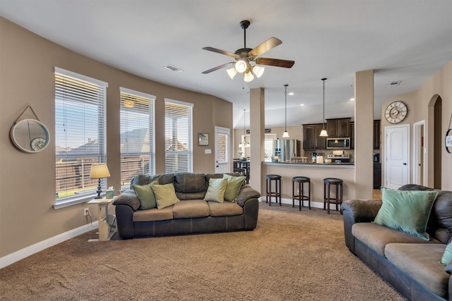 carpeted living area featuring a ceiling fan, arched walkways, visible vents, and baseboards