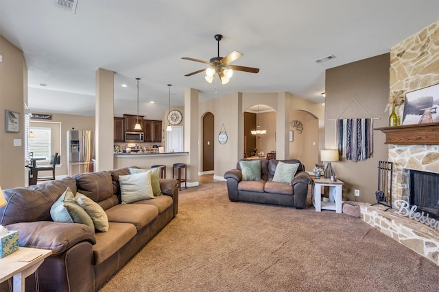 living room featuring visible vents, arched walkways, a stone fireplace, and light colored carpet