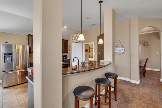 kitchen with arched walkways, stainless steel fridge with ice dispenser, visible vents, dark stone counters, and a kitchen bar