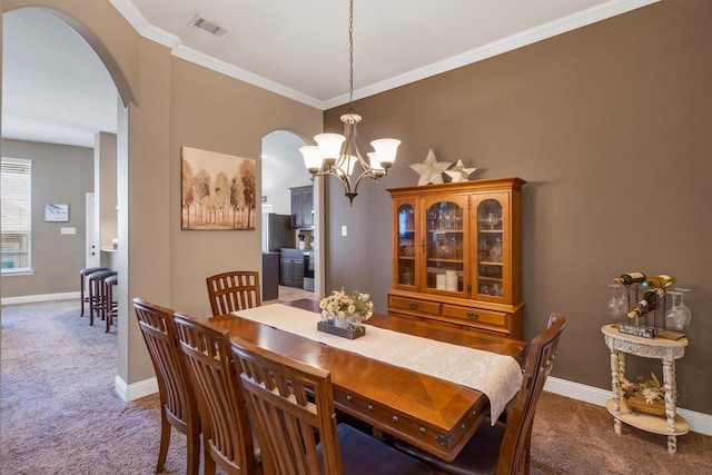 carpeted dining space with visible vents, arched walkways, baseboards, and ornamental molding