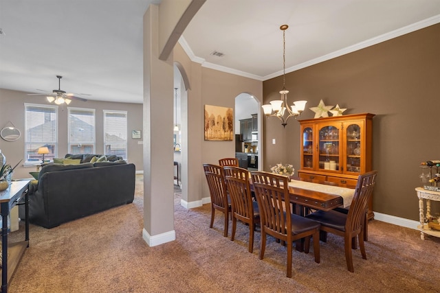 carpeted dining space with baseboards, ceiling fan with notable chandelier, arched walkways, and ornamental molding