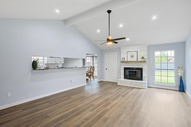 unfurnished living room featuring baseboards, a ceiling fan, wood finished floors, a stone fireplace, and beam ceiling