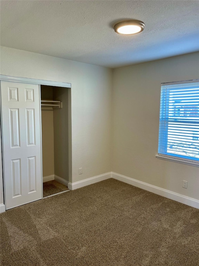 unfurnished bedroom featuring carpet floors, a closet, a textured ceiling, and baseboards