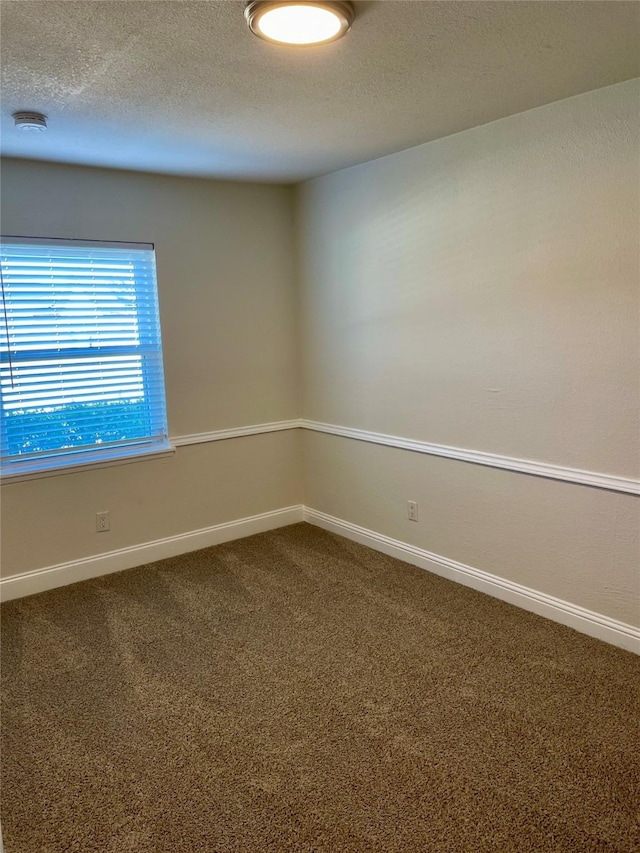 spare room with baseboards, dark colored carpet, and a textured ceiling