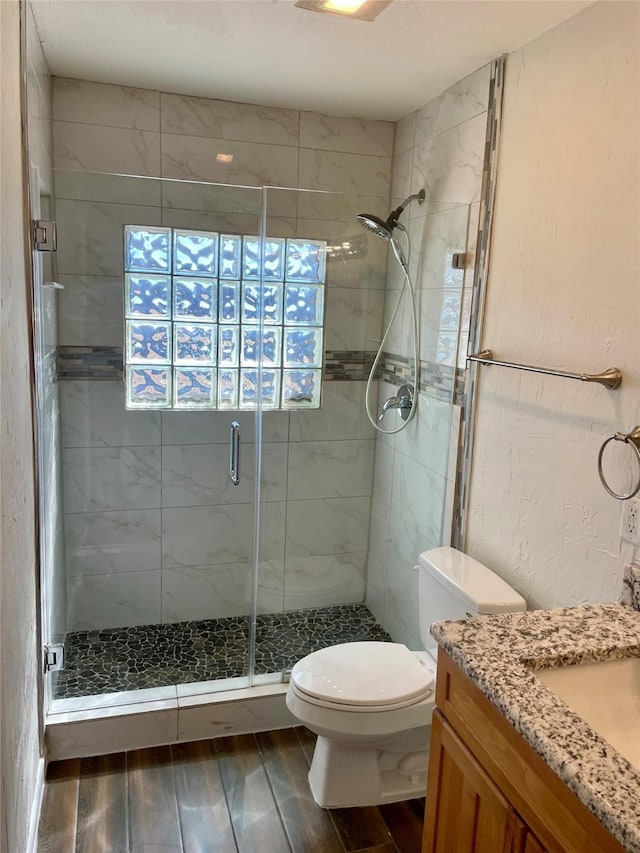 full bath featuring wood finish floors, a textured wall, toilet, a shower stall, and vanity