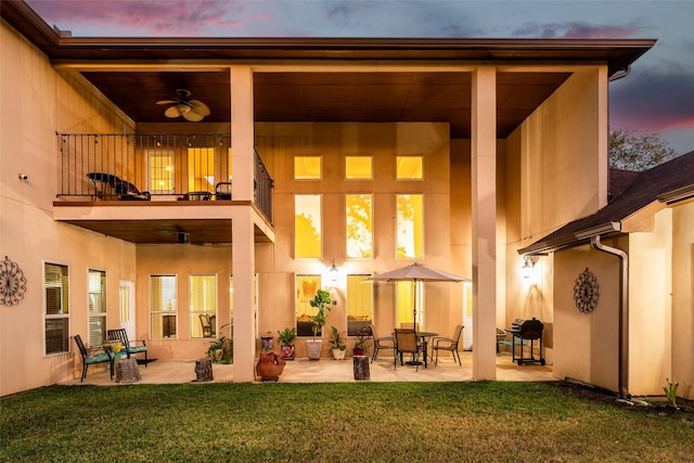 back of house with a balcony, ceiling fan, a yard, a patio area, and stucco siding