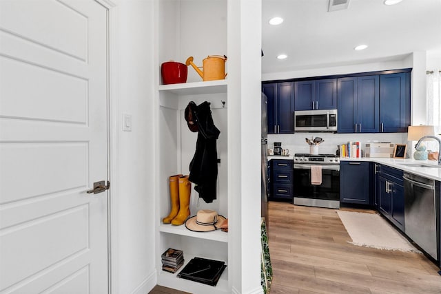 kitchen featuring blue cabinetry, light countertops, light wood-style flooring, appliances with stainless steel finishes, and a sink