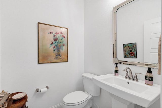 bathroom featuring toilet, baseboards, and a sink