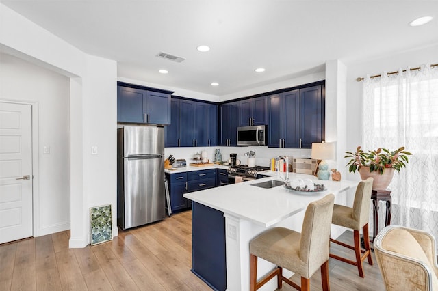 kitchen featuring visible vents, appliances with stainless steel finishes, a sink, blue cabinets, and a kitchen breakfast bar