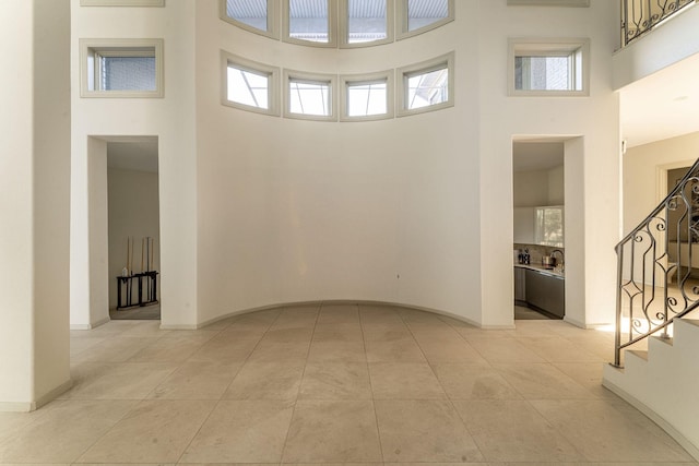 interior space featuring stairway, light tile patterned flooring, a towering ceiling, and baseboards