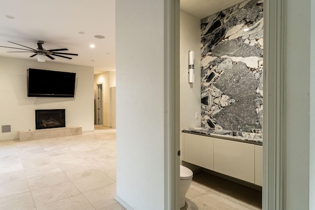 bathroom with toilet, a glass covered fireplace, ceiling fan, vanity, and tile patterned flooring