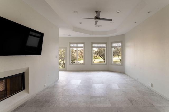 unfurnished living room featuring ceiling fan, a fireplace, visible vents, baseboards, and a tray ceiling