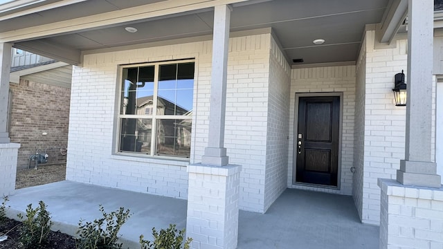 entrance to property featuring a porch and brick siding