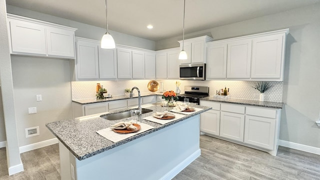 kitchen featuring a sink, white cabinets, appliances with stainless steel finishes, light wood finished floors, and decorative light fixtures