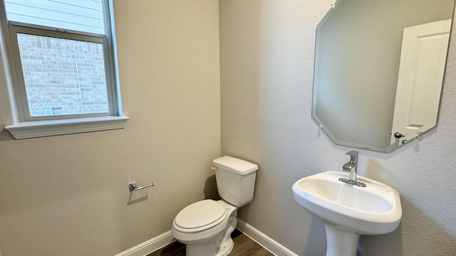 half bath with toilet, a sink, baseboards, and wood finished floors