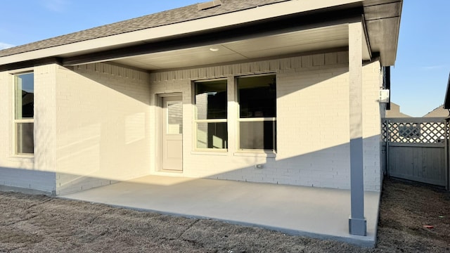 exterior space featuring a shingled roof, fence, and brick siding