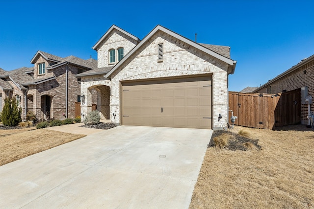 french country inspired facade featuring brick siding, driveway, an attached garage, and fence