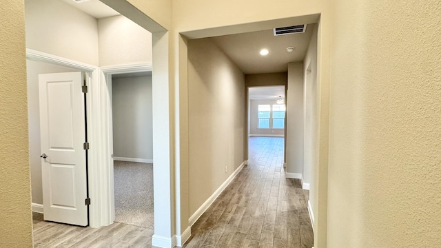 hall with visible vents, a textured wall, baseboards, and wood finished floors