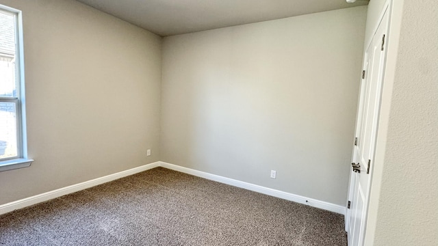 empty room featuring dark colored carpet and baseboards