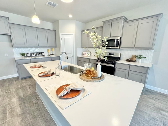 kitchen with a center island with sink, visible vents, gray cabinetry, appliances with stainless steel finishes, and a sink