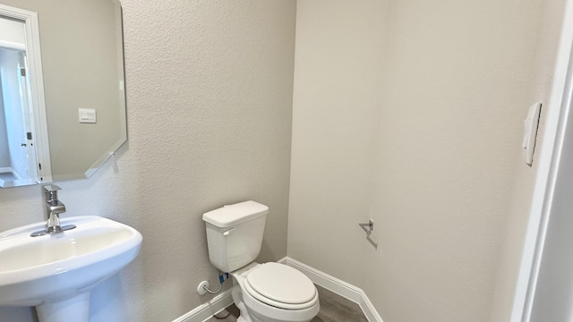 half bath with a textured wall, a sink, toilet, and baseboards