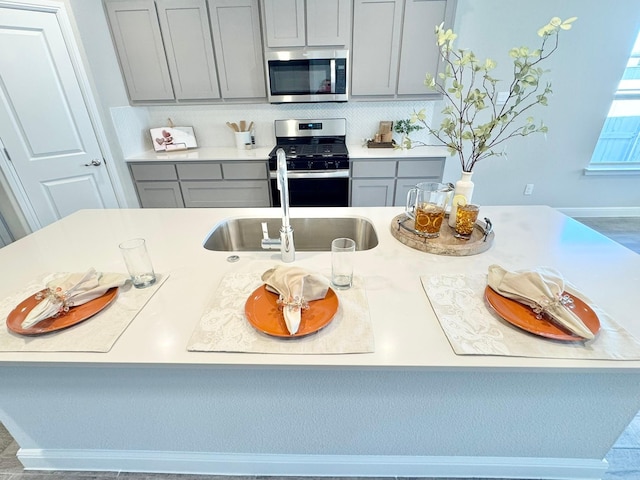 kitchen featuring a sink, light countertops, appliances with stainless steel finishes, backsplash, and gray cabinets