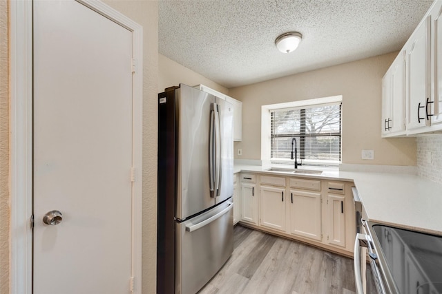 kitchen with stainless steel appliances, light countertops, a sink, a textured ceiling, and light wood-type flooring