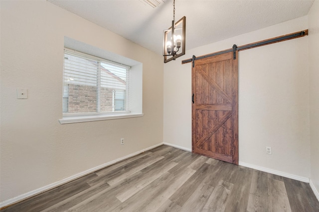 unfurnished room featuring a barn door, baseboards, and wood finished floors