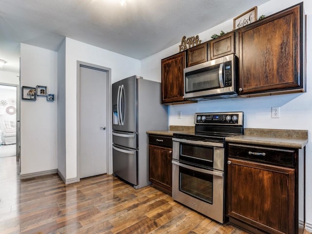 kitchen featuring appliances with stainless steel finishes, dark brown cabinetry, and wood finished floors