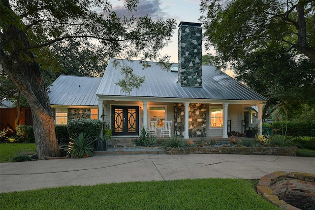 view of front facade featuring stone siding, metal roof, a chimney, and covered porch