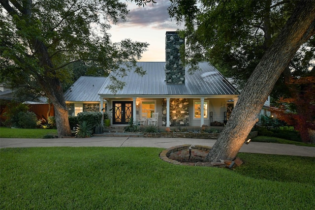 view of front of home featuring metal roof, a porch, a lawn, and a chimney