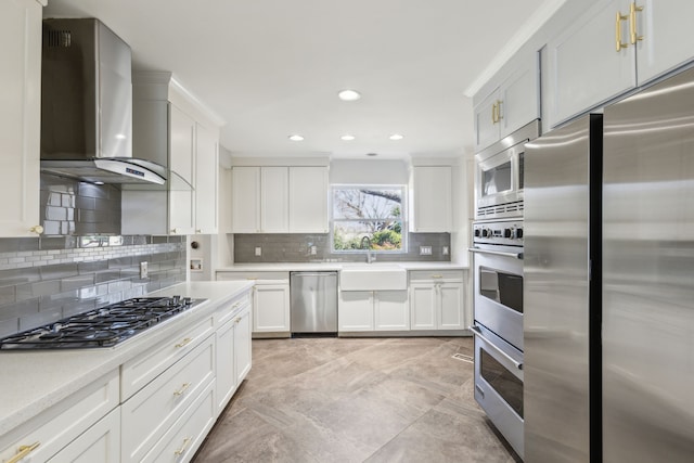 kitchen featuring light countertops, decorative backsplash, appliances with stainless steel finishes, a sink, and wall chimney exhaust hood