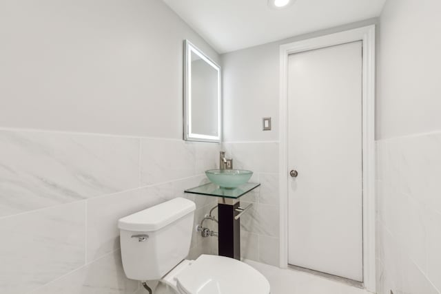 half bathroom featuring toilet, tile walls, and a sink