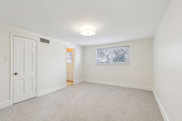 unfurnished bedroom with light carpet, ensuite bath, visible vents, and baseboards