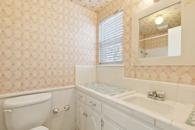 bathroom featuring a shower, toilet, wainscoting, vanity, and wallpapered walls