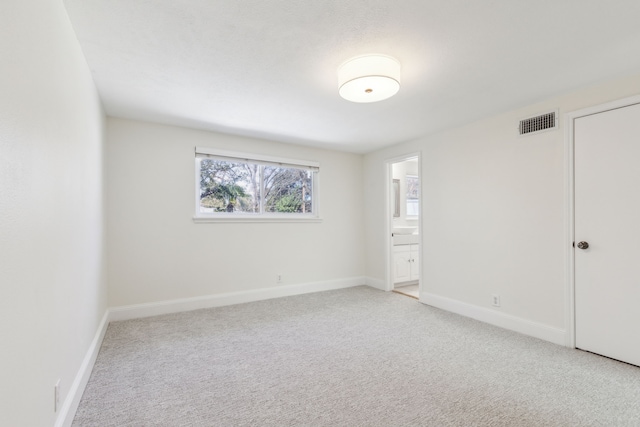 unfurnished bedroom featuring ensuite bath, baseboards, visible vents, and light colored carpet