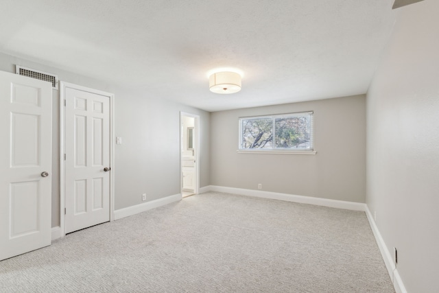 unfurnished bedroom featuring ensuite bath, carpet, visible vents, and baseboards