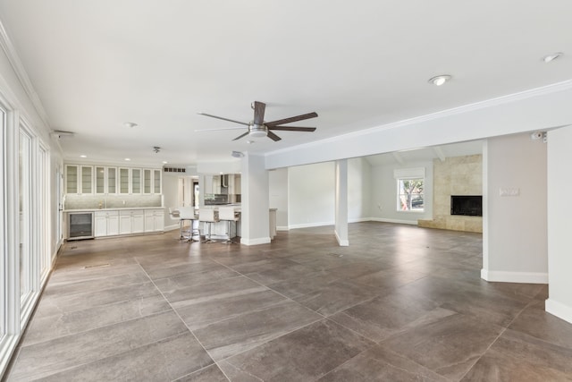 unfurnished living room with baseboards, ceiling fan, wine cooler, ornamental molding, and a premium fireplace