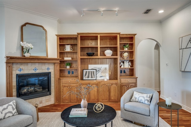 living area with visible vents, arched walkways, a tiled fireplace, wood finished floors, and crown molding