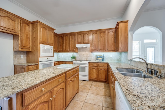 kitchen featuring under cabinet range hood, white appliances, a sink, light stone countertops, and brown cabinetry