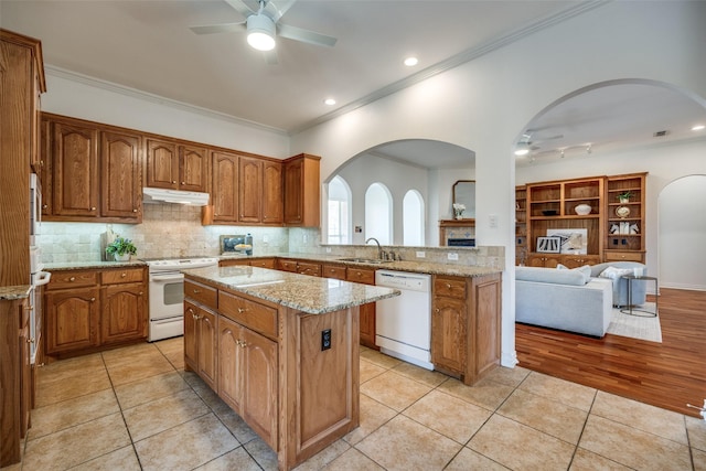 kitchen featuring white appliances, light tile patterned floors, a kitchen island, under cabinet range hood, and a sink