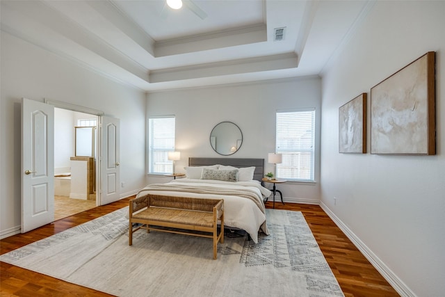 bedroom featuring baseboards, visible vents, wood finished floors, a tray ceiling, and crown molding