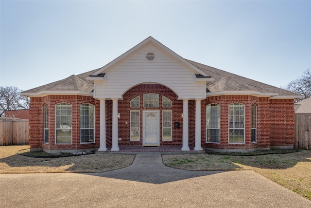 view of front facade with brick siding, a shingled roof, and fence