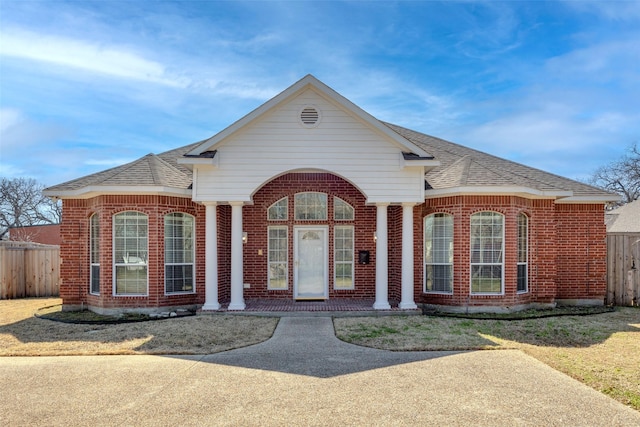 view of front of property with a shingled roof, fence, and brick siding